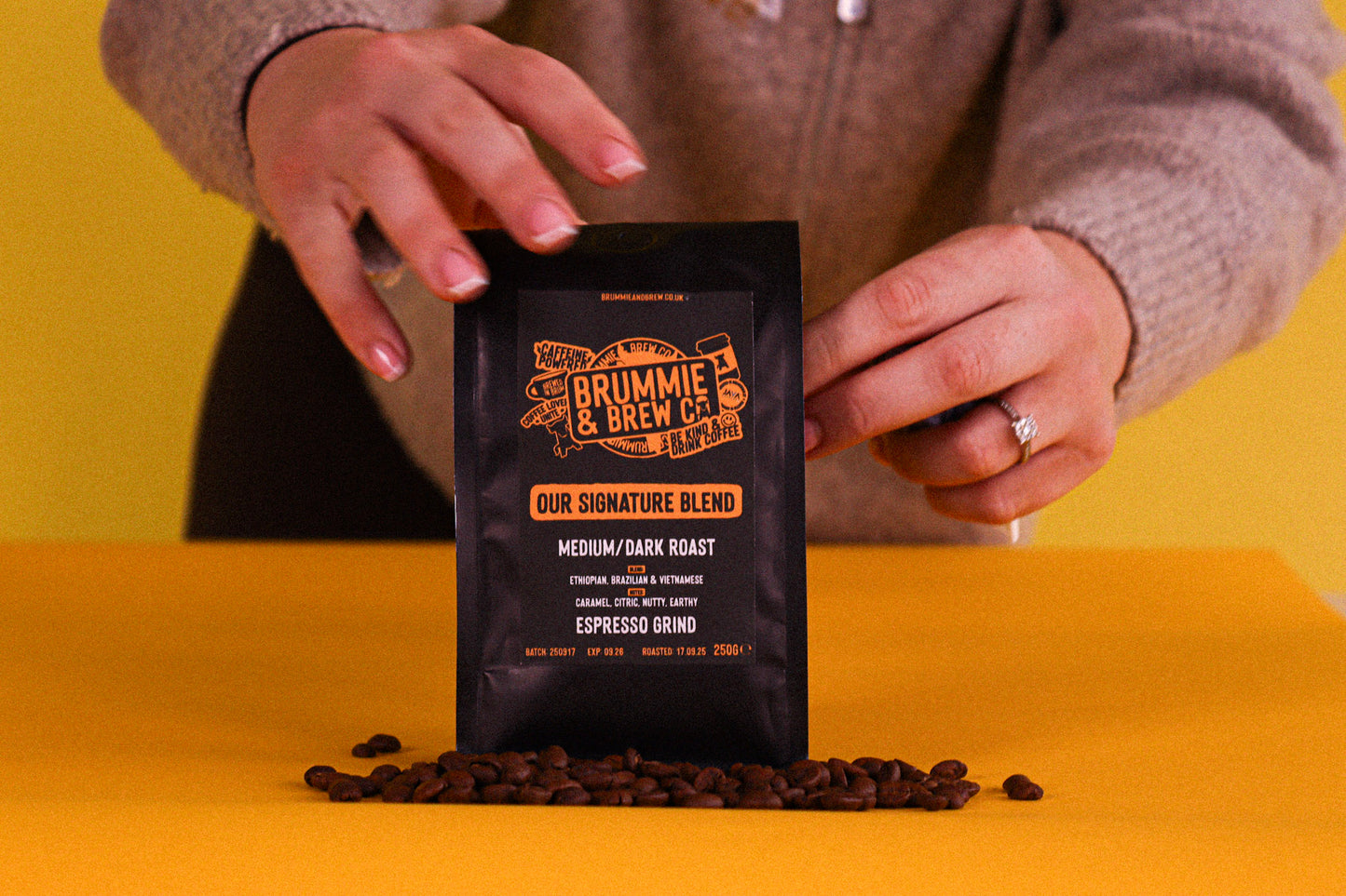 Person holding a black coffee bag of espresso grind coffee labeled 'Brummie & Brew Co.' on a yellow background